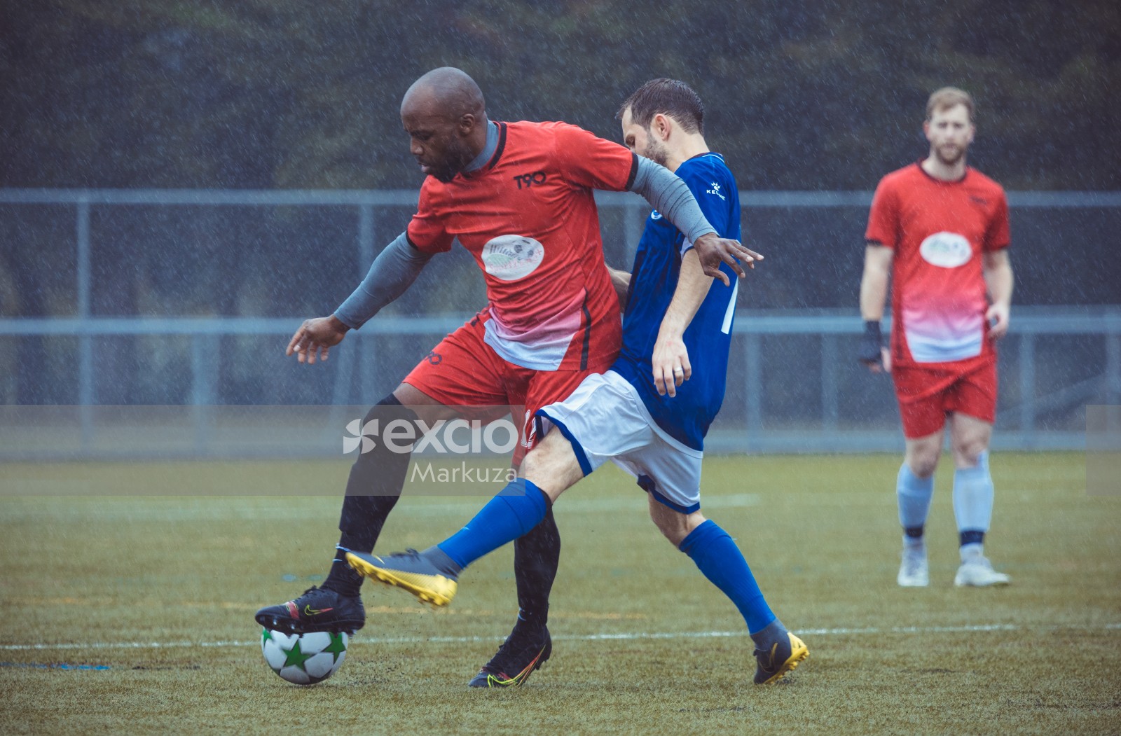 Player in blue shirt tackling opponent in red shirt in the rain - Sports Zone sunday league