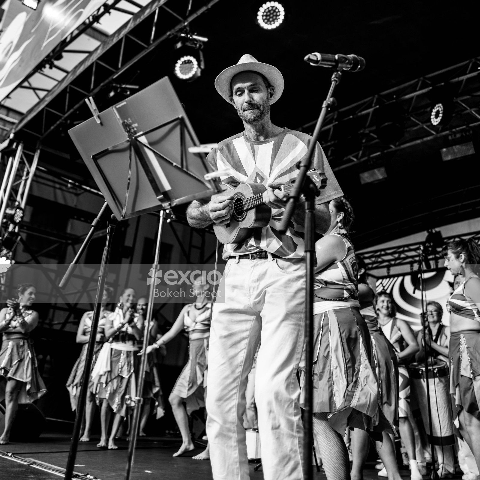 Dance performers and a man play ukulele on stage at Cuba Dupa 2021 B&W
