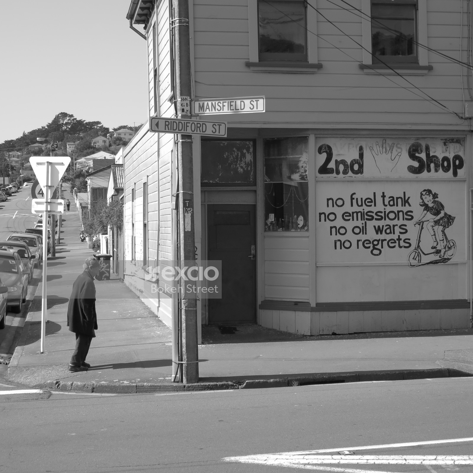 Old man on a secluded sidewalk next to a second hand shop in Newtown black and white