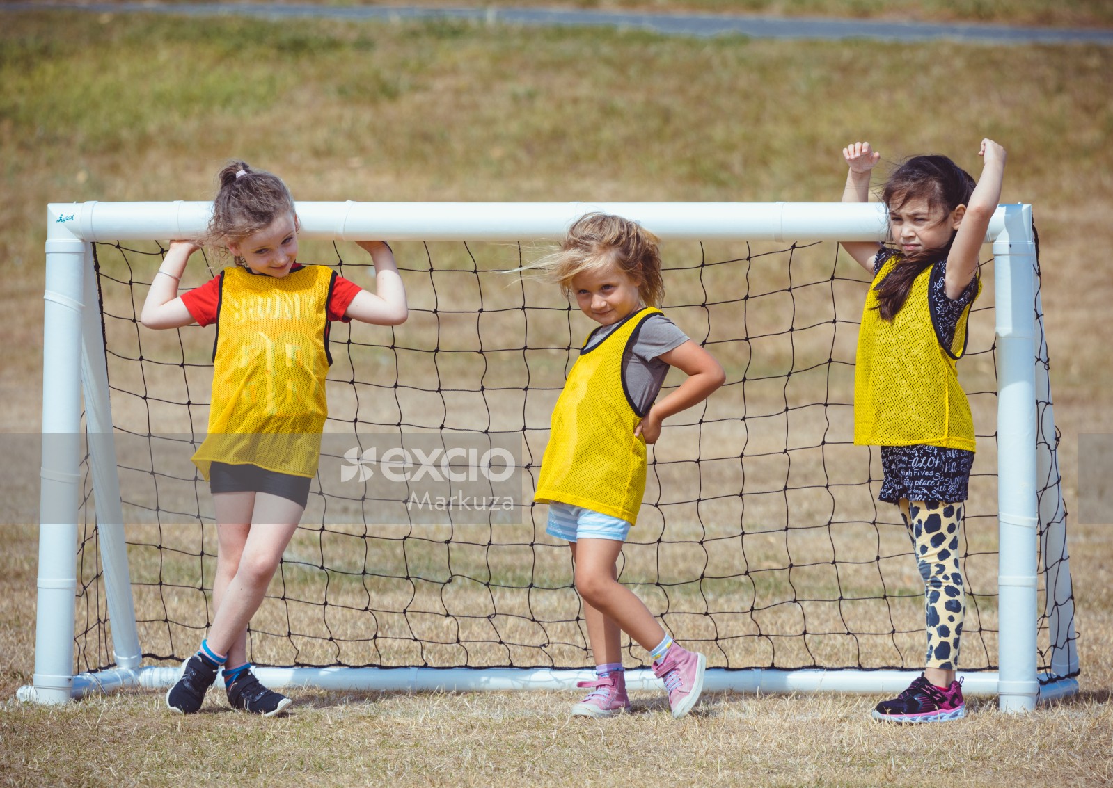 Three little girls in yellow scrimmage vests at a goal post - Little Dribblers