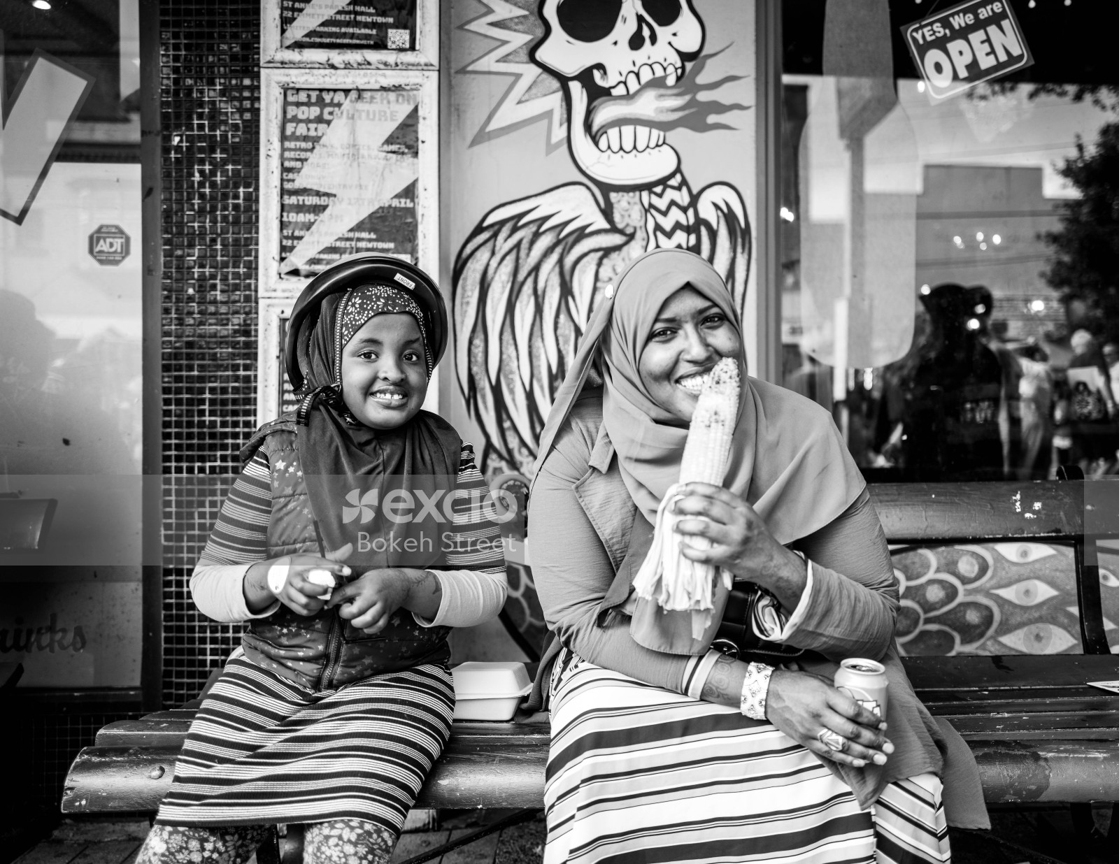 Hijab wearing mother and daughter on a bench eating corn at Newtown festival 2021 black and white