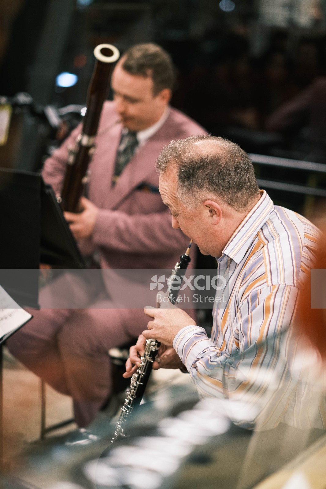 People playing clarinet and bassoon at a concert in striped shirt and pink suit