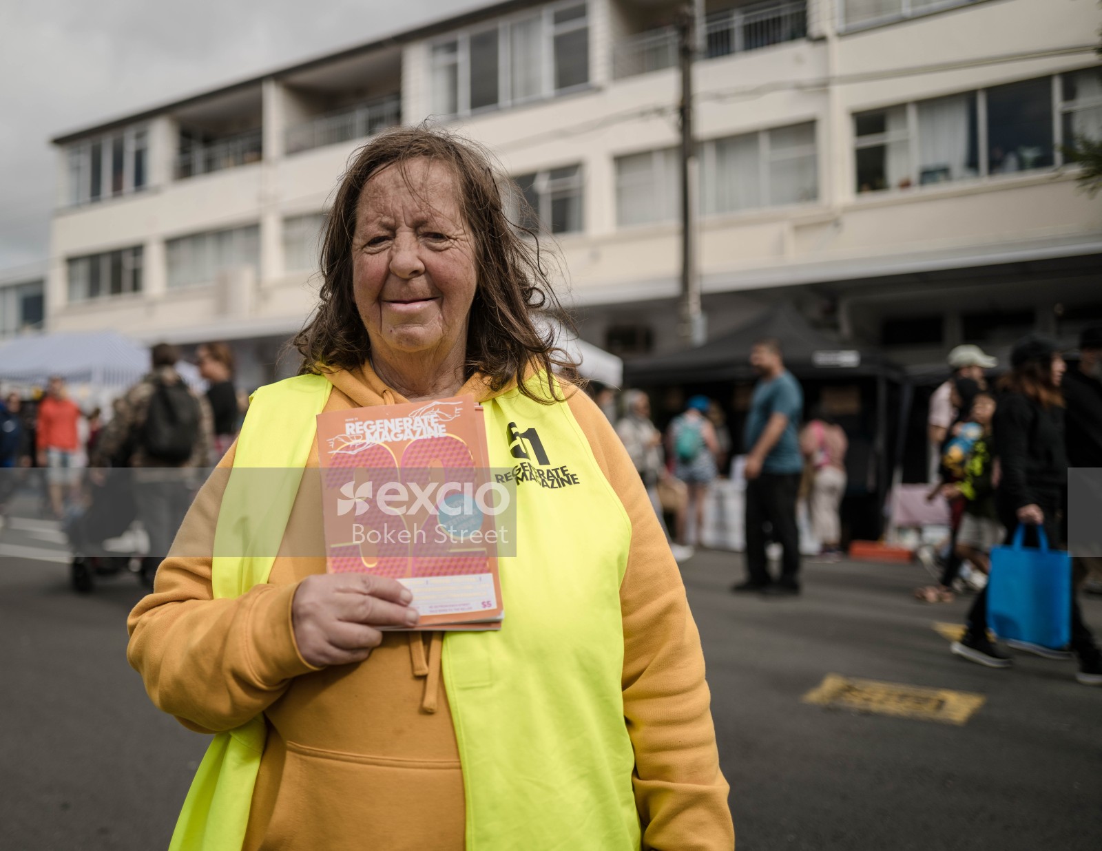 Woman wearing a yellow vest and orange hoodie holding a Regenerate magazine at Newtown festival 2021