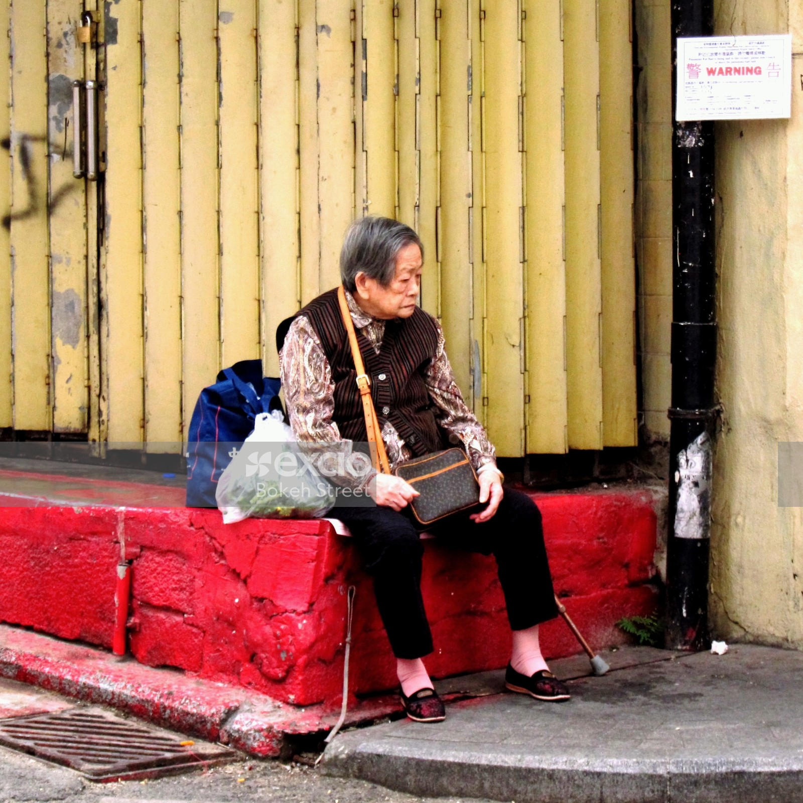 Old lady sitting on a platform in the street in Hong Kong